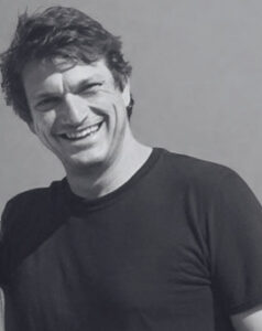 A man with dark hair and a black top smiles at the camera