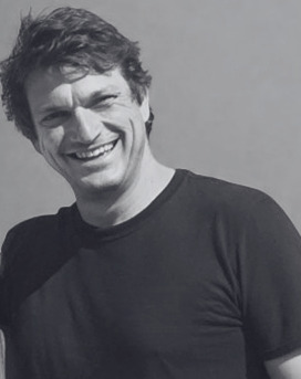 A man with dark hair and a black top smiles at the camera
